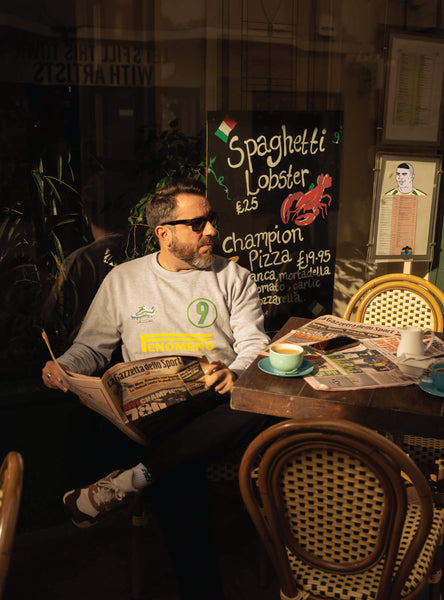 Man sitting at a table at an italian restaurant wearing a Ronaldo 9 sweatshirt with a menu board behind him