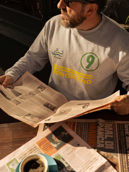 Man reading a newspaper at a table wearing a Ronaldo 9 seatshirt with a blurred background
