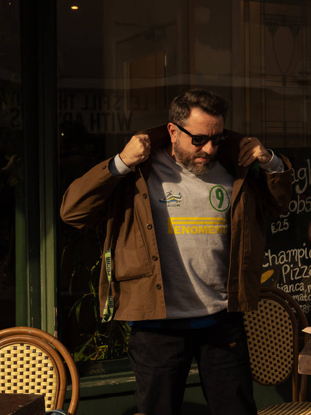 Man wearing sunglasses, a jacket and Ronaldo 9 sweatshirt in front of a store window with reflections.